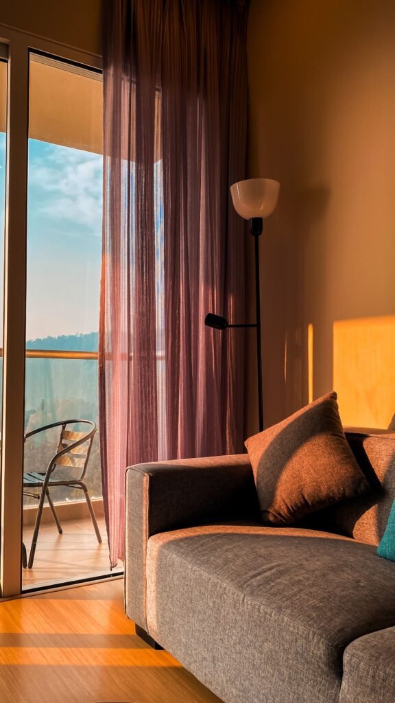 Warm sunlight fills a modern indoor space with a cozy sofa and balcony view.