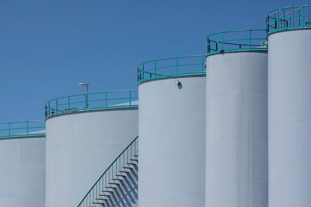 Large industrial storage tanks with green railings against a clear blue sky.